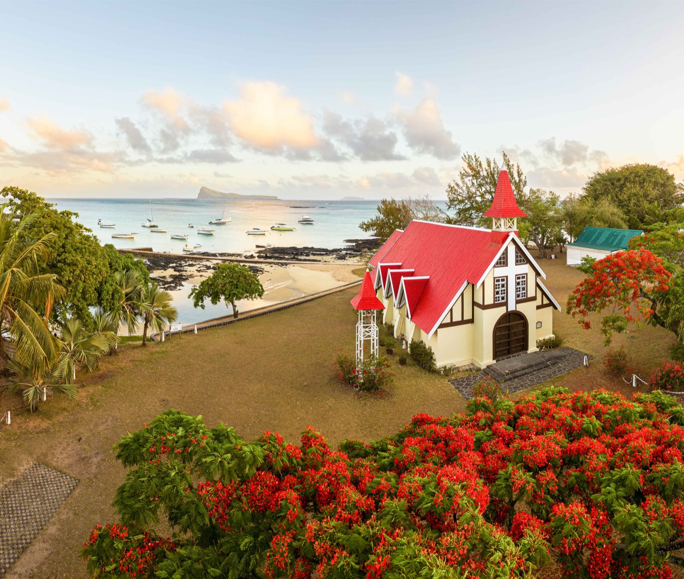 Église rouge au bord de l'eau à Cap Malheureux, avec des bateaux et des fleurs colorées