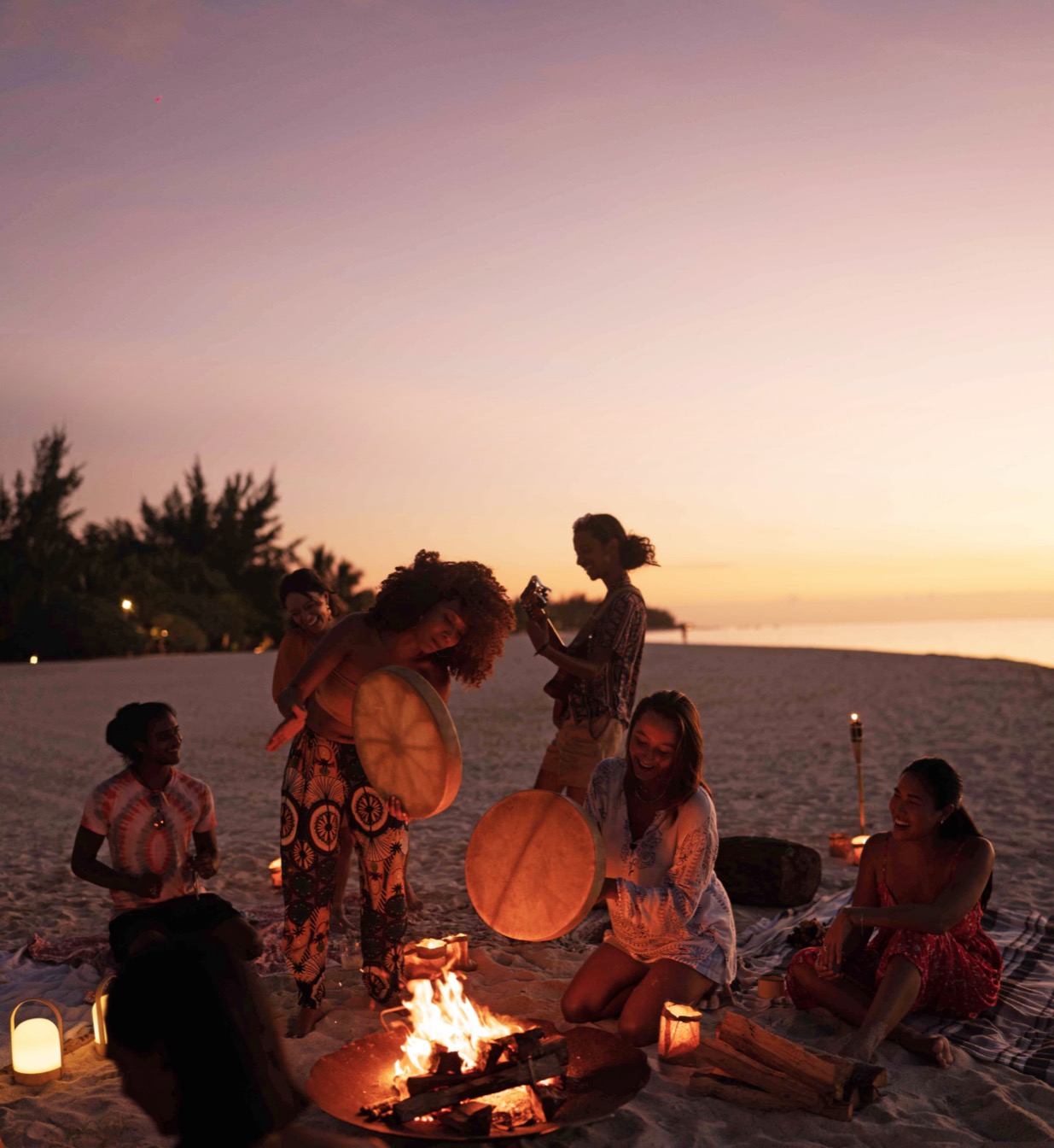 Célébration sur la plage au coucher du soleil, avec musique et feu de camp, et des participants engagés.