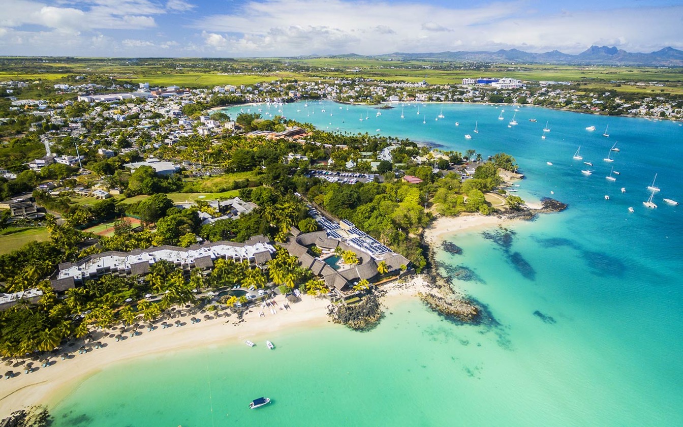 Vue panoramique de Grand Baie avec plages de sable et lagon turquoise entouré de villas et voiliers.
