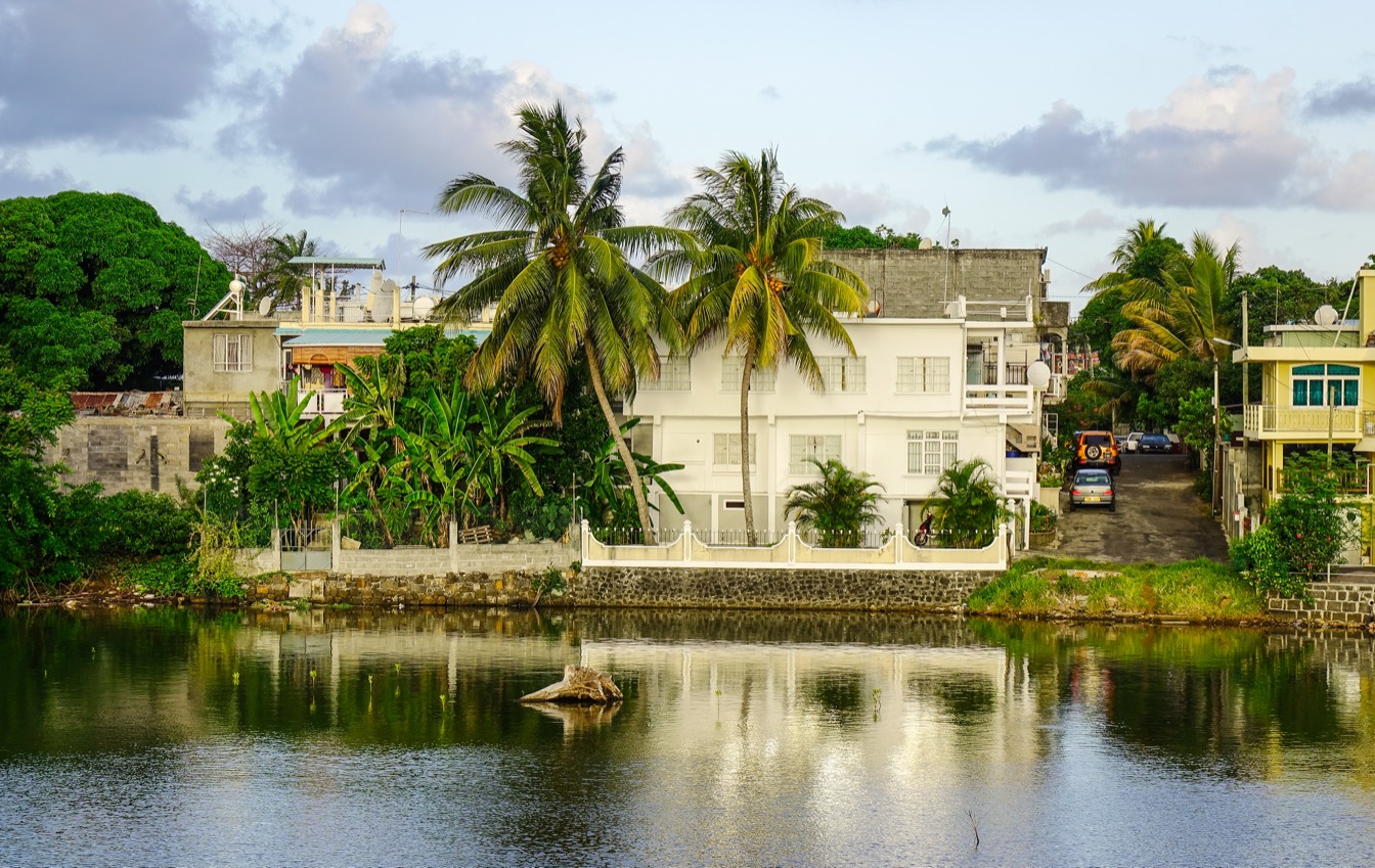 Vue de la rivière à Mahébourg, maisons bordées de palmiers et verdure luxuriante
