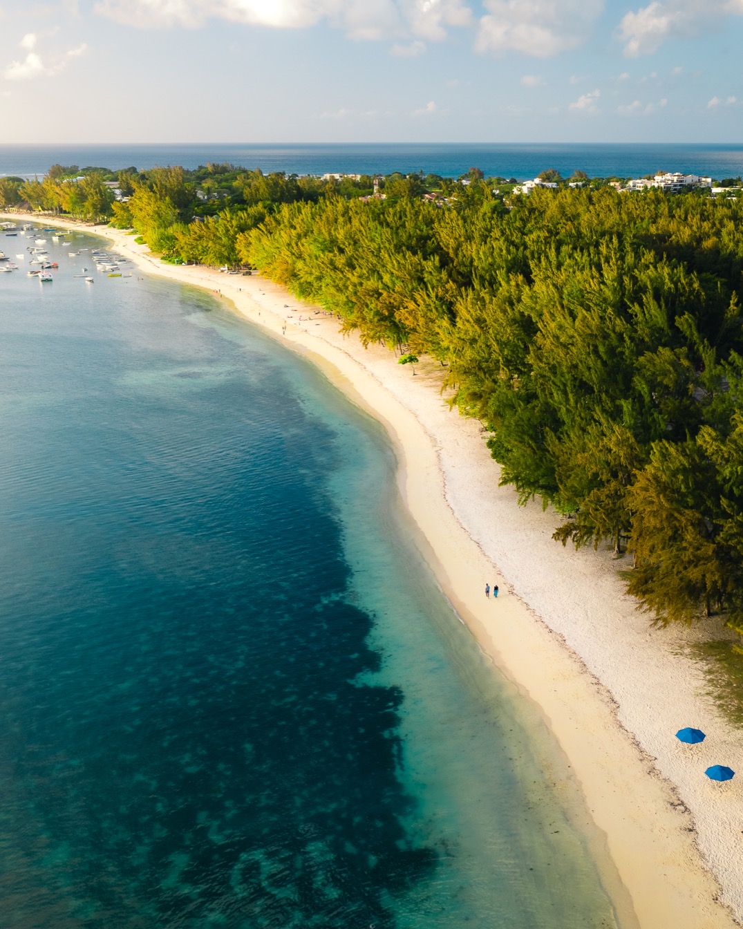 Plage de Mont Choisy, sable fin, eau turquoise, palmiers et bateaux.