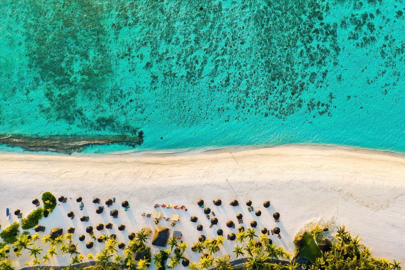 Vue aérienne de la plage de Pereybère, sable blanc et eau turquoise, serviettes et palmiers.