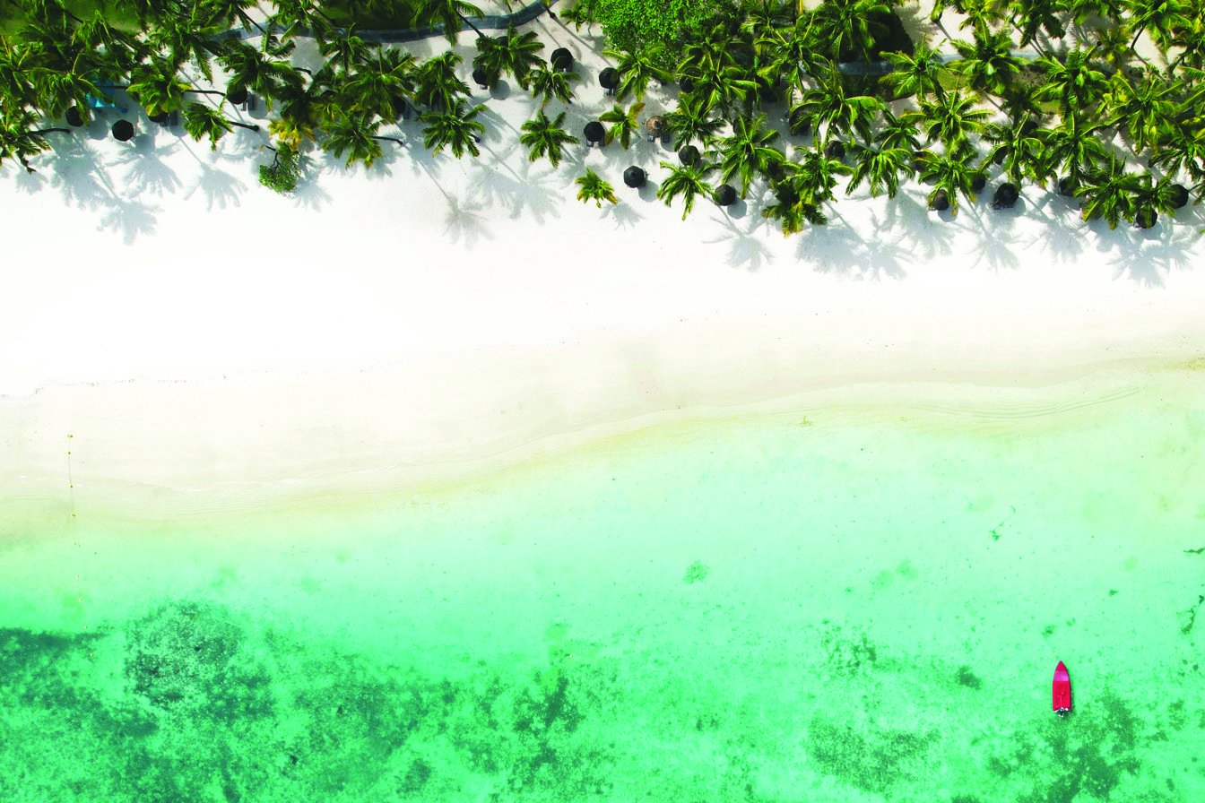 Vue aérienne d'une plage secrète avec palmiers et un bateau rouge sur l'eau turquoise